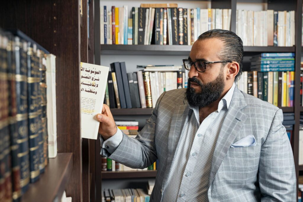 Man in a suit reading a book in a well-stocked library, emphasizing knowledge and sophistication.